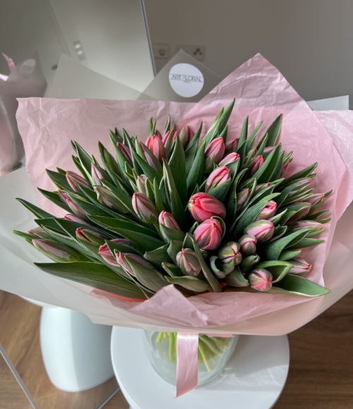 Blumenstrauß mit hellrosa Tulpen in weiß-rosafarbener Verpackung