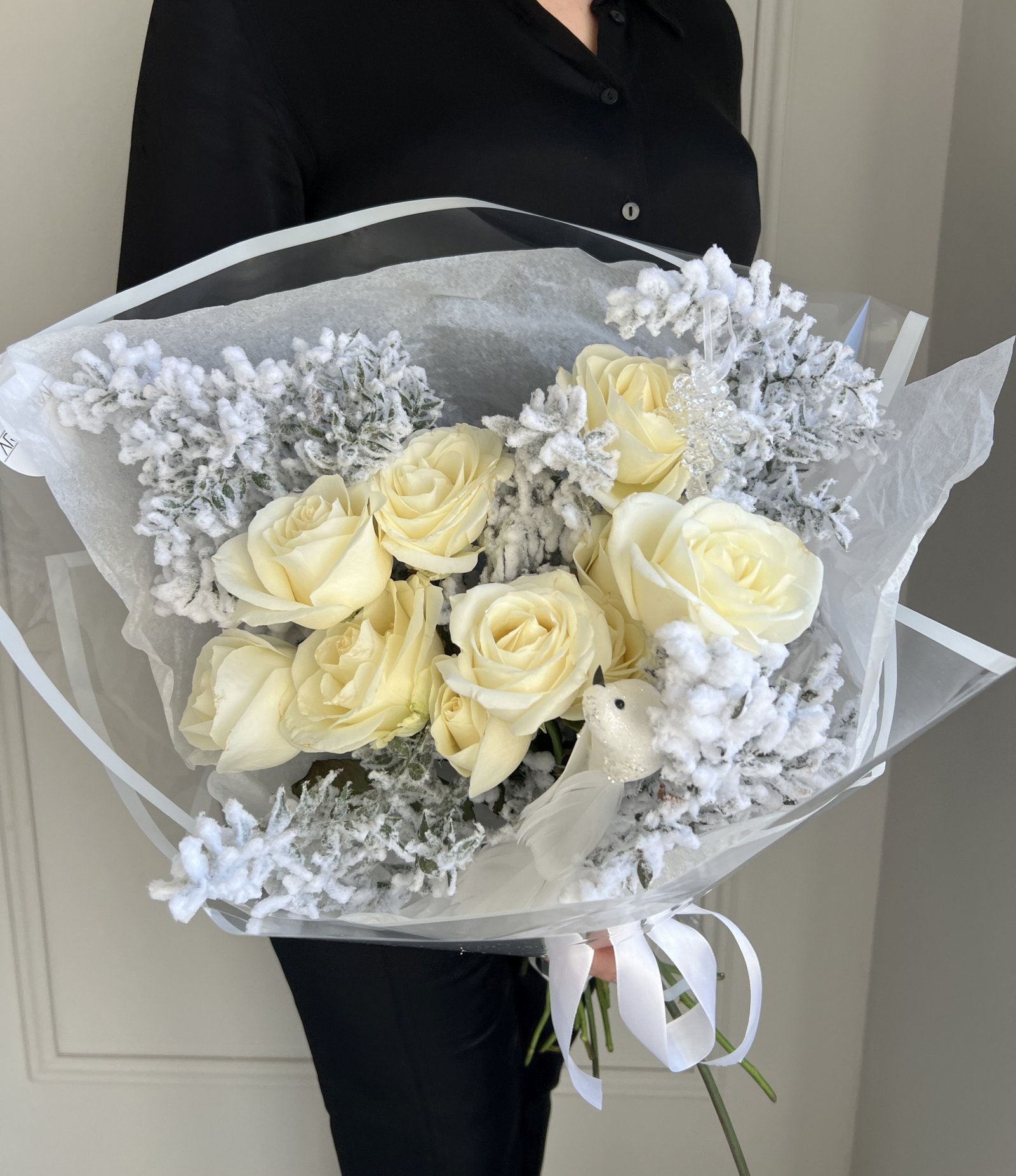 Weißer Blumenstrauß mit Rosen, verschneitem Ruscus und weißer Vogel-Dekoration.