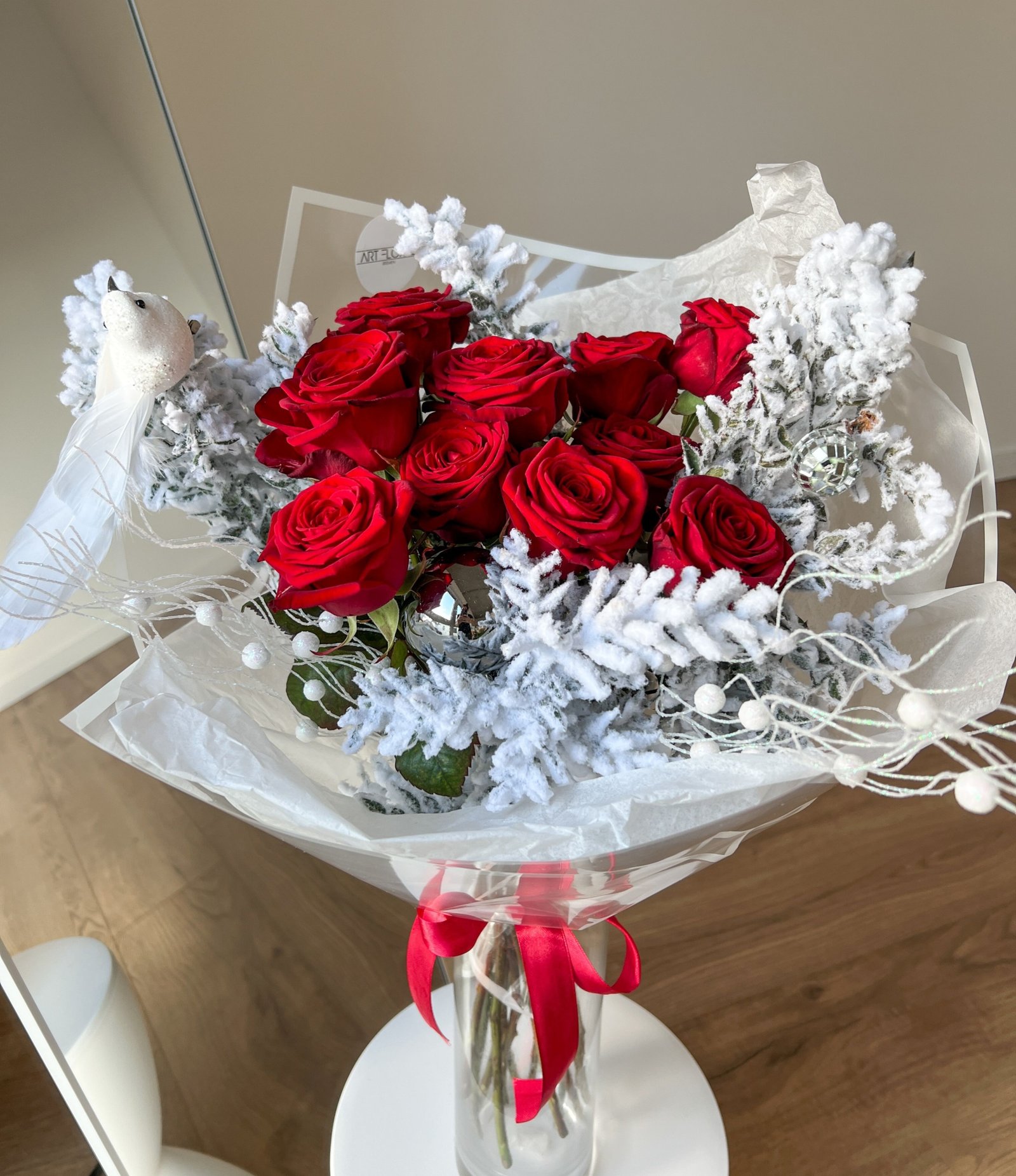Blumenstrauß „Winterrose“ mit roten Rosen und verschneiten weißen Ruscuszweigen.