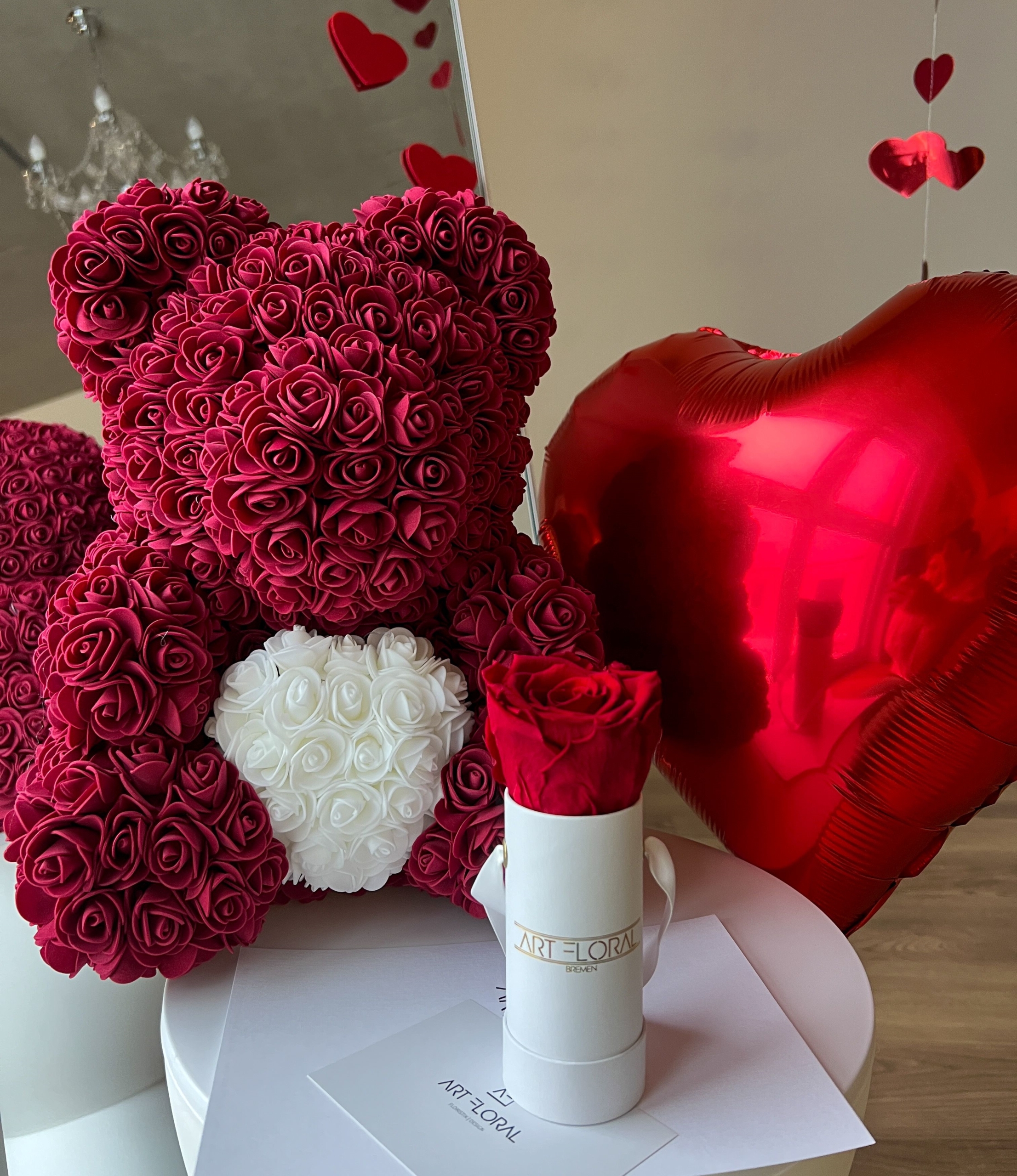Geschenkset Bordeaux Love Bordeauxfarbener Rosenbär mit weißem Herz neben weißer Box mit Ewiger Rose und rotem Herzballon