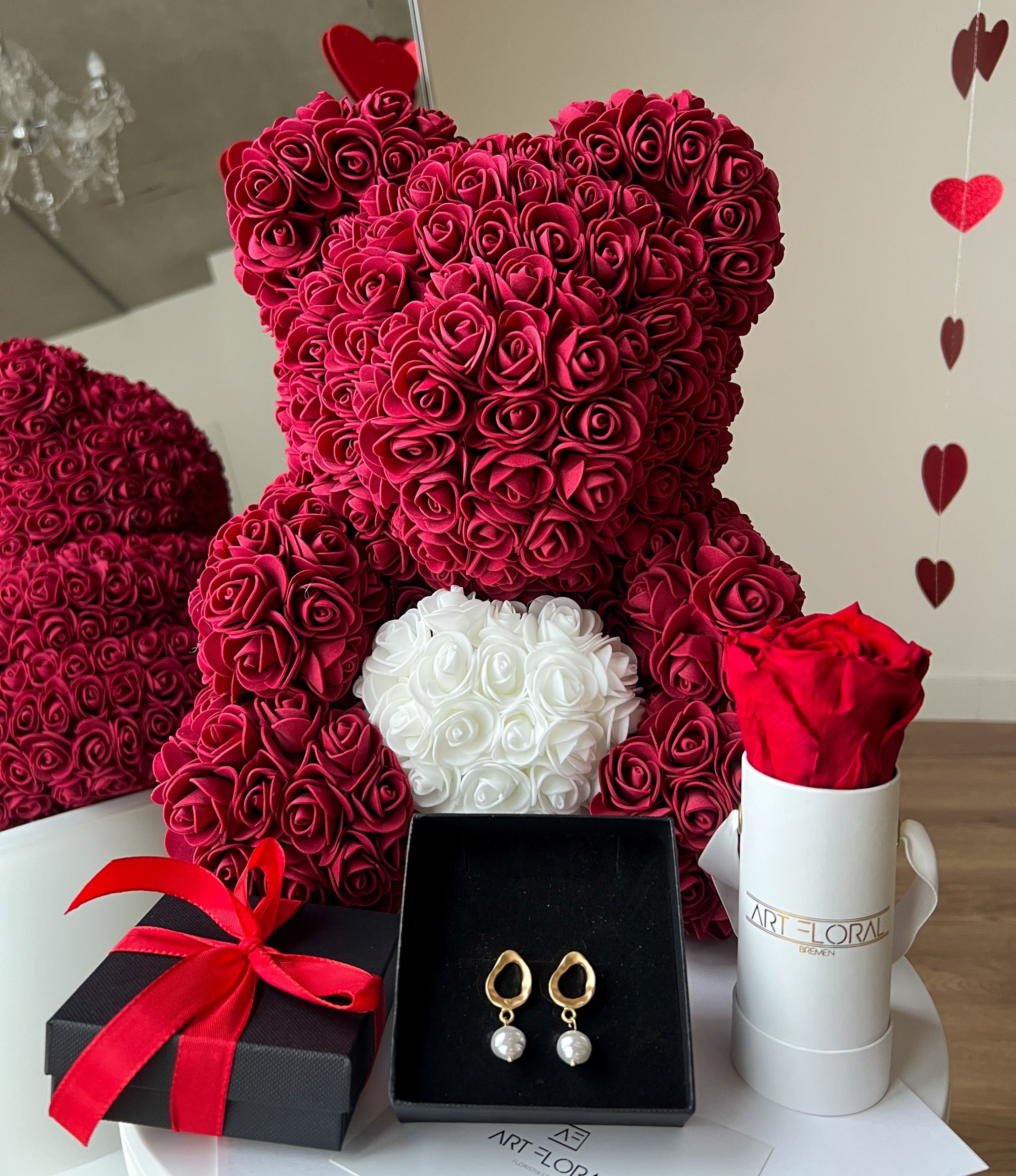 Geschenkset Bordeaux Pearl Bordeauxfarbener Rosenbär mit weißem Herz neben weißer Mini-Box mit Ewiger Rose und Perlen-Ohrsteckern