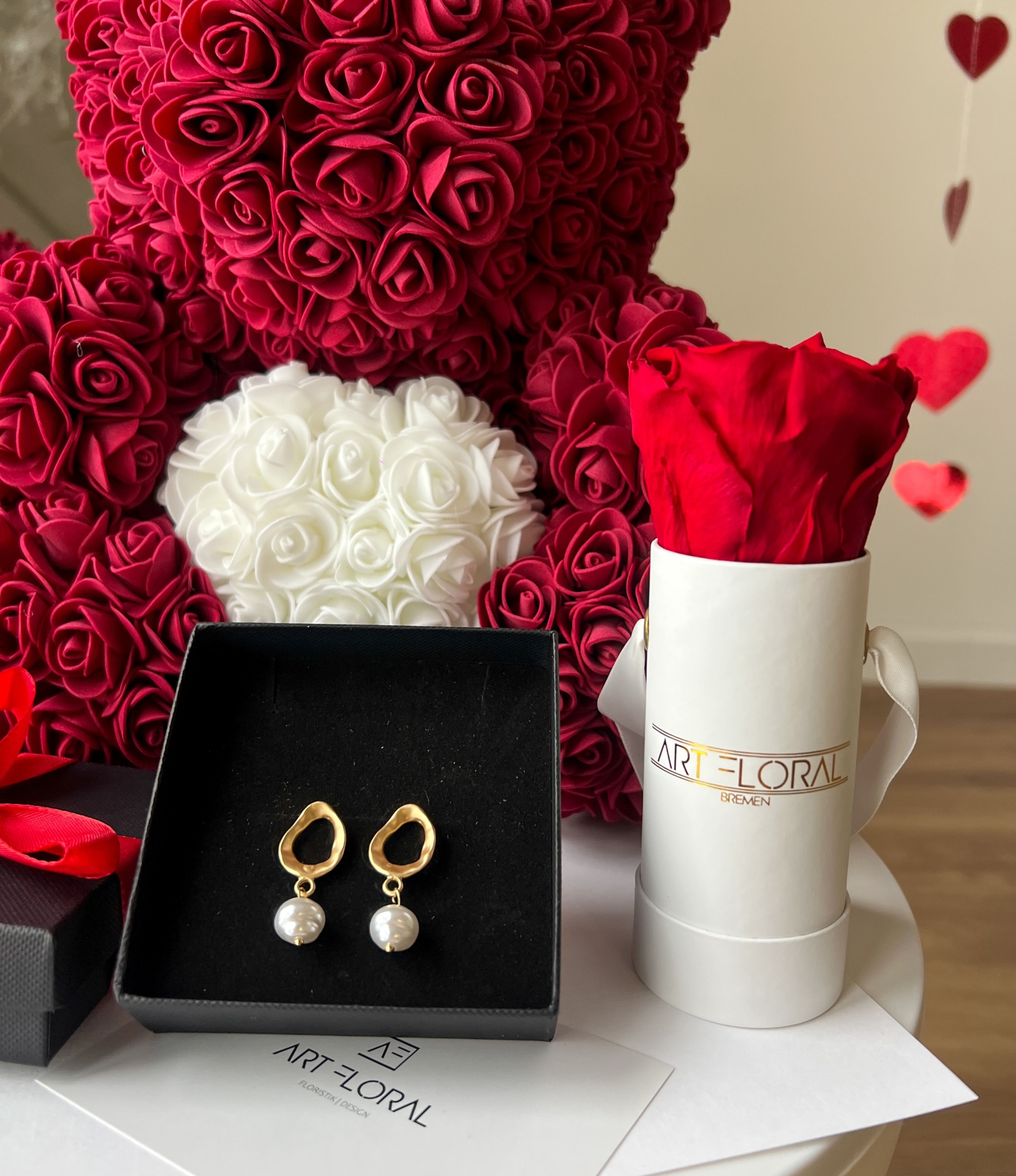 Geschenkset Bordeaux Pearl Bordeauxfarbener Rosenbär mit weißem Herz neben weißer Mini-Box mit Ewiger Rose und Perlen-Ohrsteckern